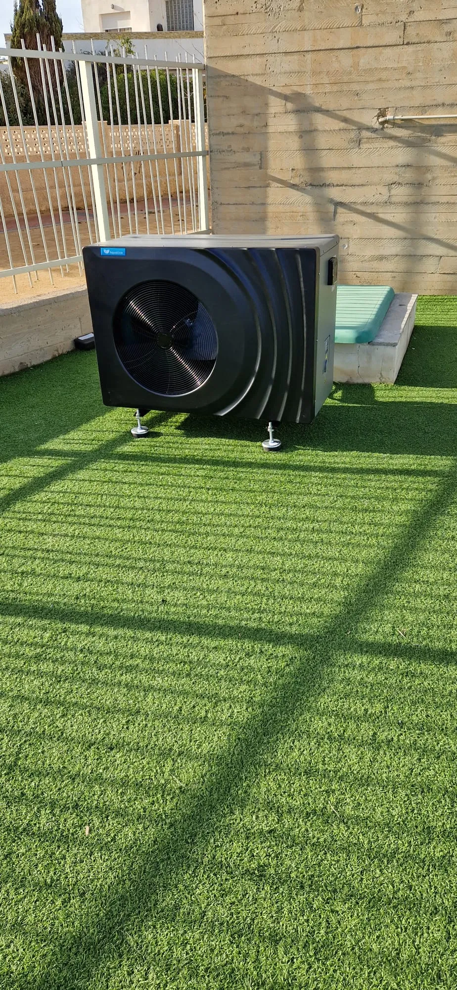 Bomba de calor negra instalada en una terraza con césped artificial