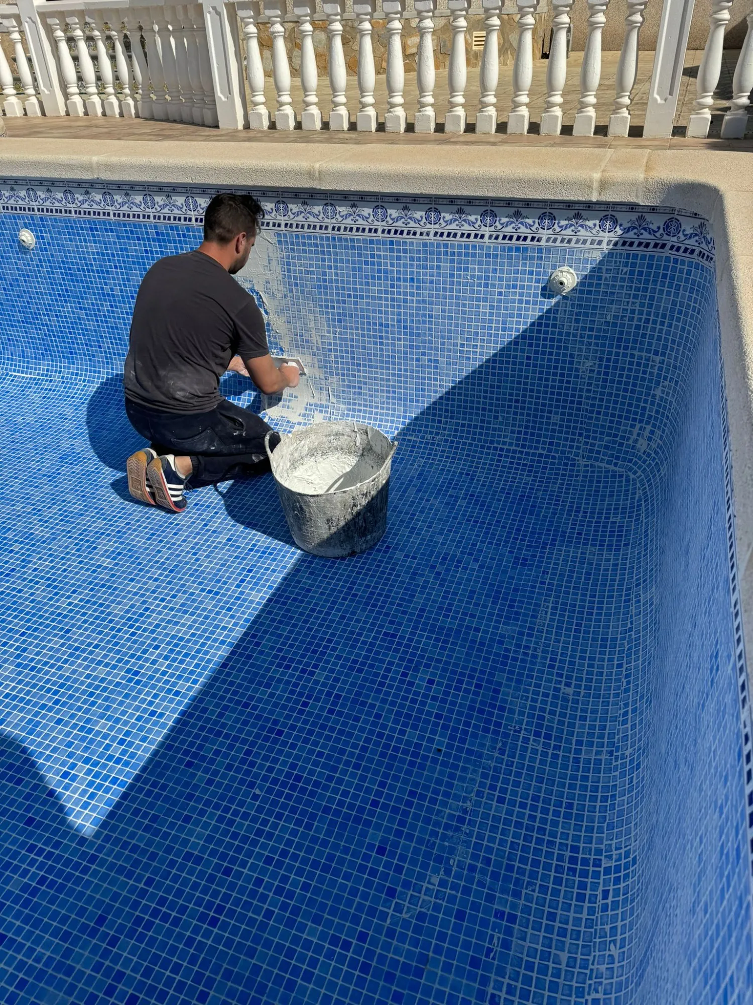 Operario de Neopool aplicando lechada nueva en el gresite azul de una piscina vacía